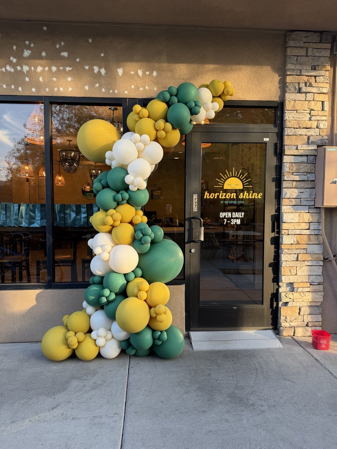 Green, yellow, and white balloon garland framing the Horizon Shine storefront