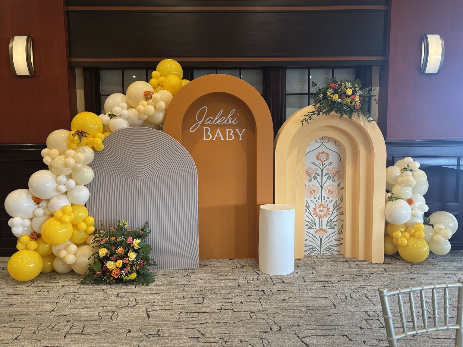 Jalebi Baby shower backdrop with ivory and yellow balloons, layered arches, and florals